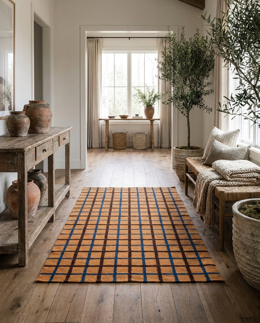 Rustic entryway with a plaid rug, wooden console table, potted olive tree, and bench in a warm, minimalist home interior.