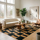 Modern living room with a cream bouclé sofa, geometric black and tan rug, wooden coffee table, and minimalist decor.