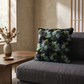 Modern living room with a dark textured sofa, patterned punch needle pillow, wooden coffee table, and dried floral vase.