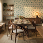Modern dining room with a wooden table, clover wallpaper, floating shelves, and warm ambient lighting.