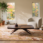Modern living room with a walnut coffee table, cream boucle armchair, and abstract rug, featuring autumn forest views.