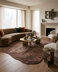 Modern living room with a curved brown velvet sofa, textured floral rug, brass coffee table, and minimalist fireplace.