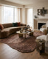 Modern living room with a curved brown velvet sofa, textured floral rug, brass coffee table, and minimalist fireplace.