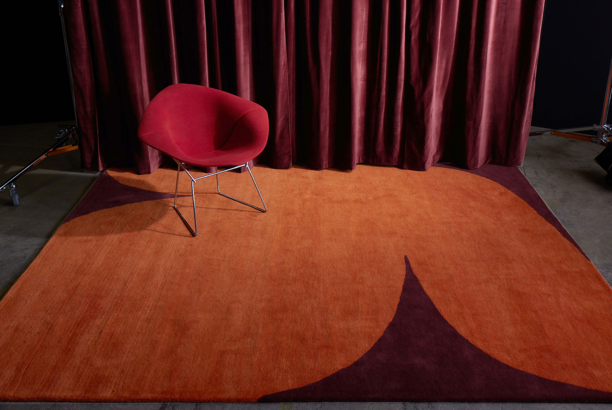 A red stage curtain next to an orange red, hand tufted area rug called, Dove Love by Angela Adams