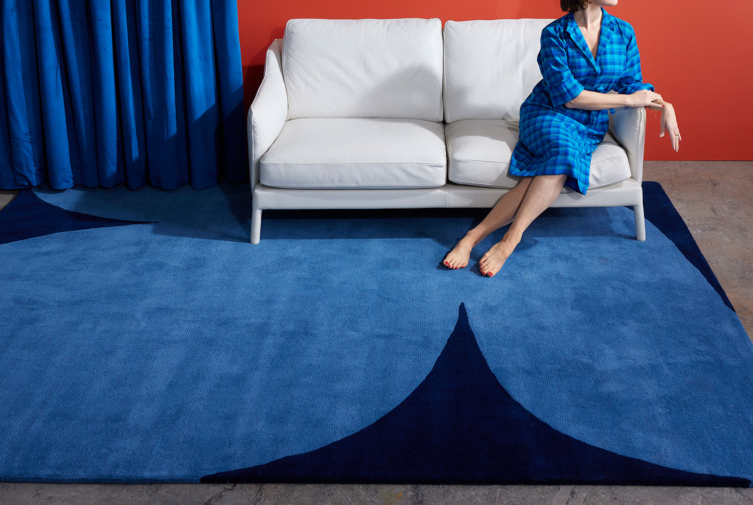 A woman in a blue check dress sits on a hand tufted area rug called, Dove Midnight by Angela Adams