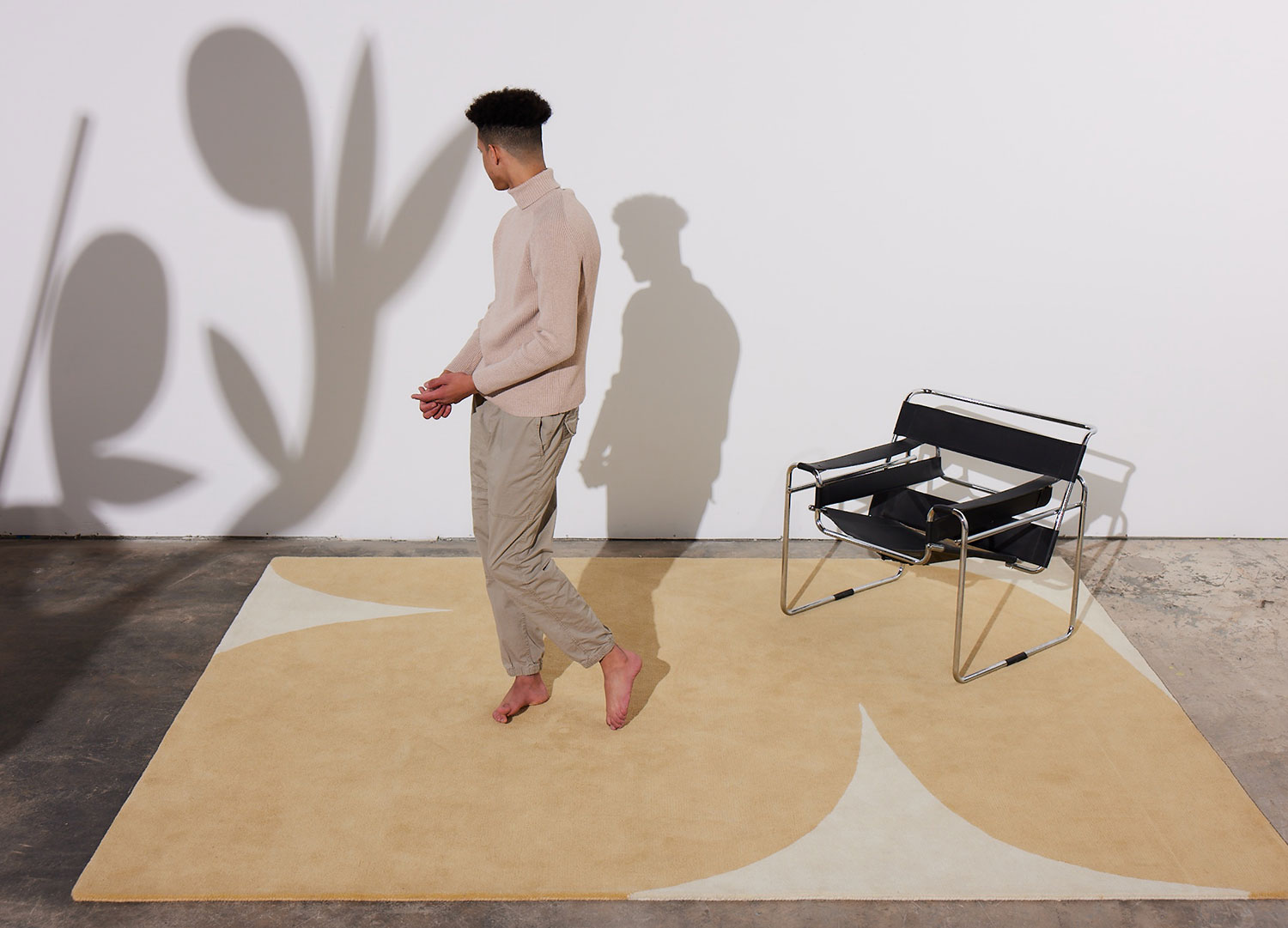 A man in tan colors looks at his shadow on a a Beige hand tufted area rug called Dove Peace by angela adams