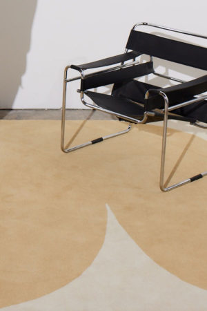 A black, and metal chair sits on a beige and cream colored area rug by Angela Adams