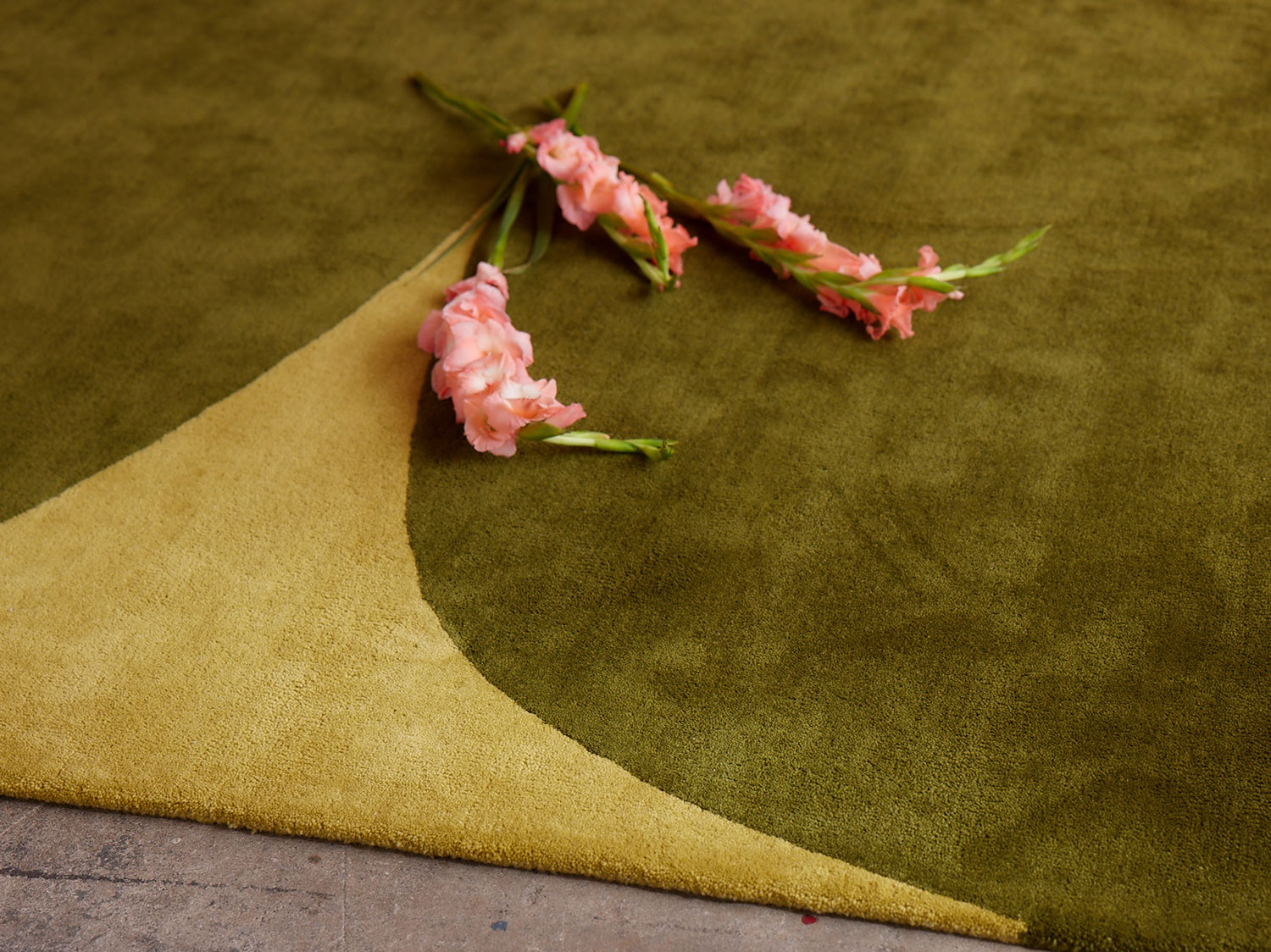 Pink flowers rest on a green, hand tufted rug called Dove Rainforest by angela adams