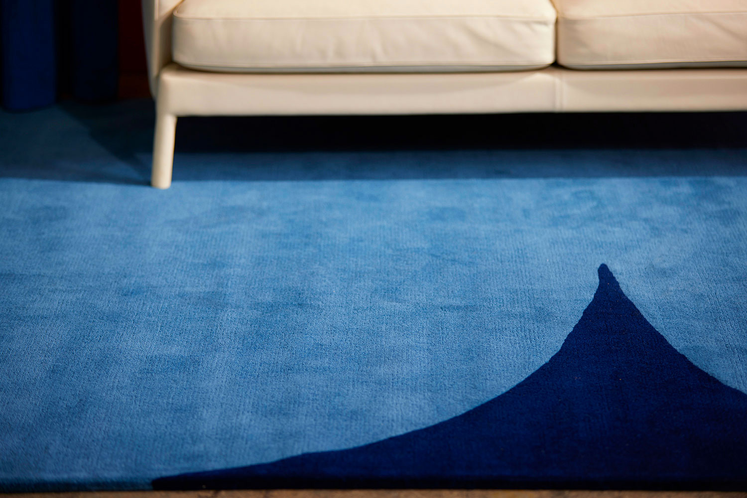 A white couch positioned on top of a bold blue and dark blue, hand tufted area rug by Angela Adams, called Dove Midnight