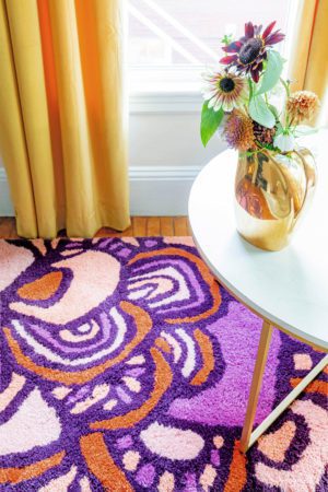A sunny room with flowers on a table sitting on a red, and pink floral pattern, modern area rug called Maeve Tulip