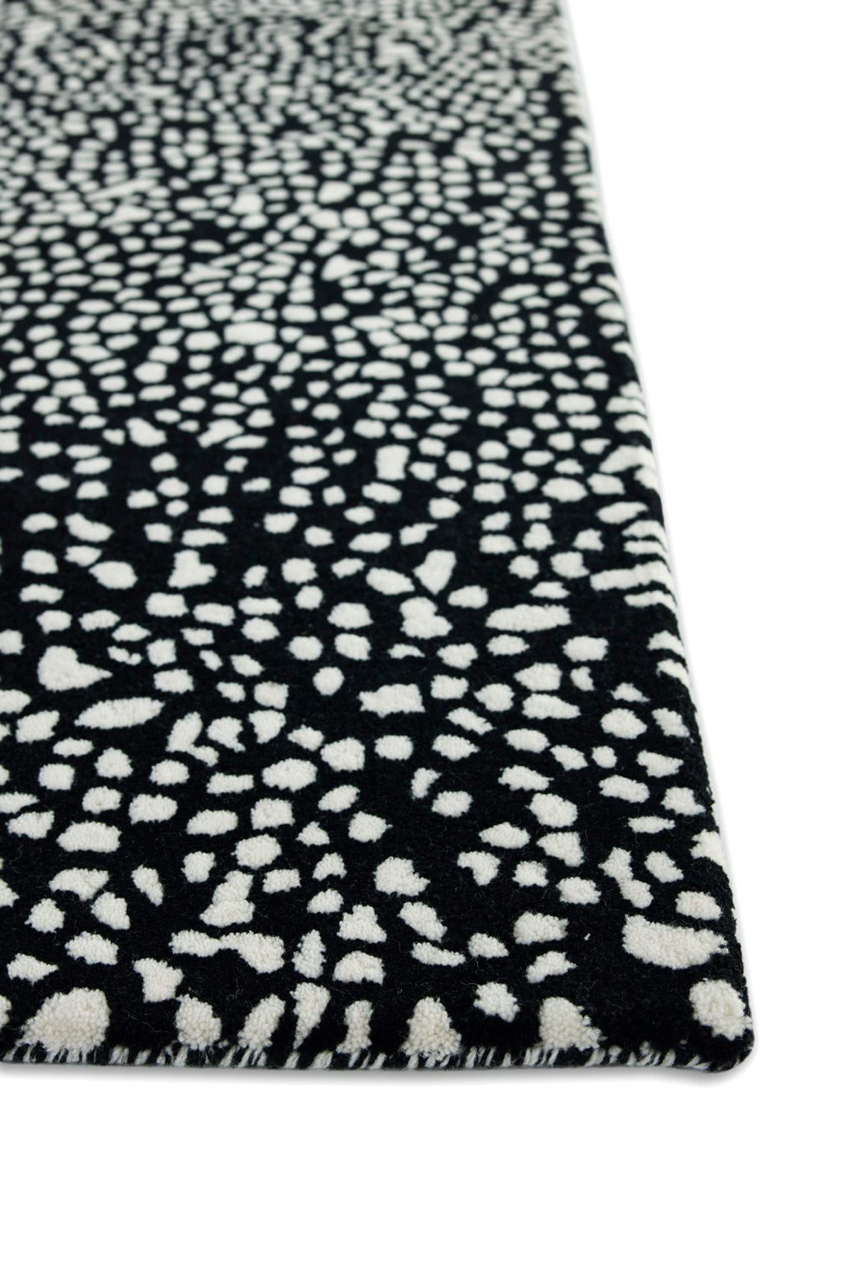 A corner detail of a black and white speckled area rug called Starry Onyx by Angela Adams