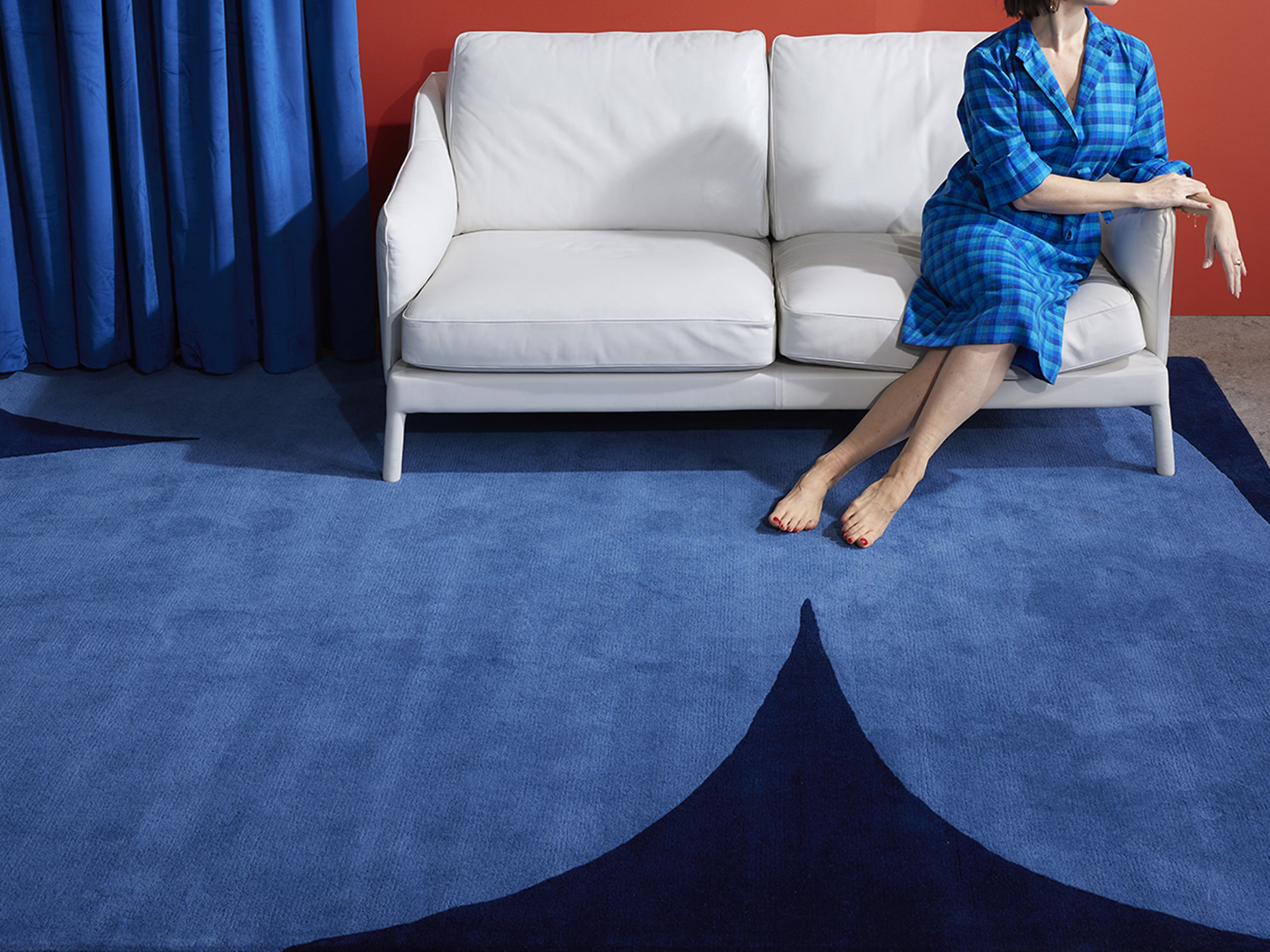 A woman in a blue dress sits casually on a white leather couch over a blue, modern area rug called Dove Twilight
