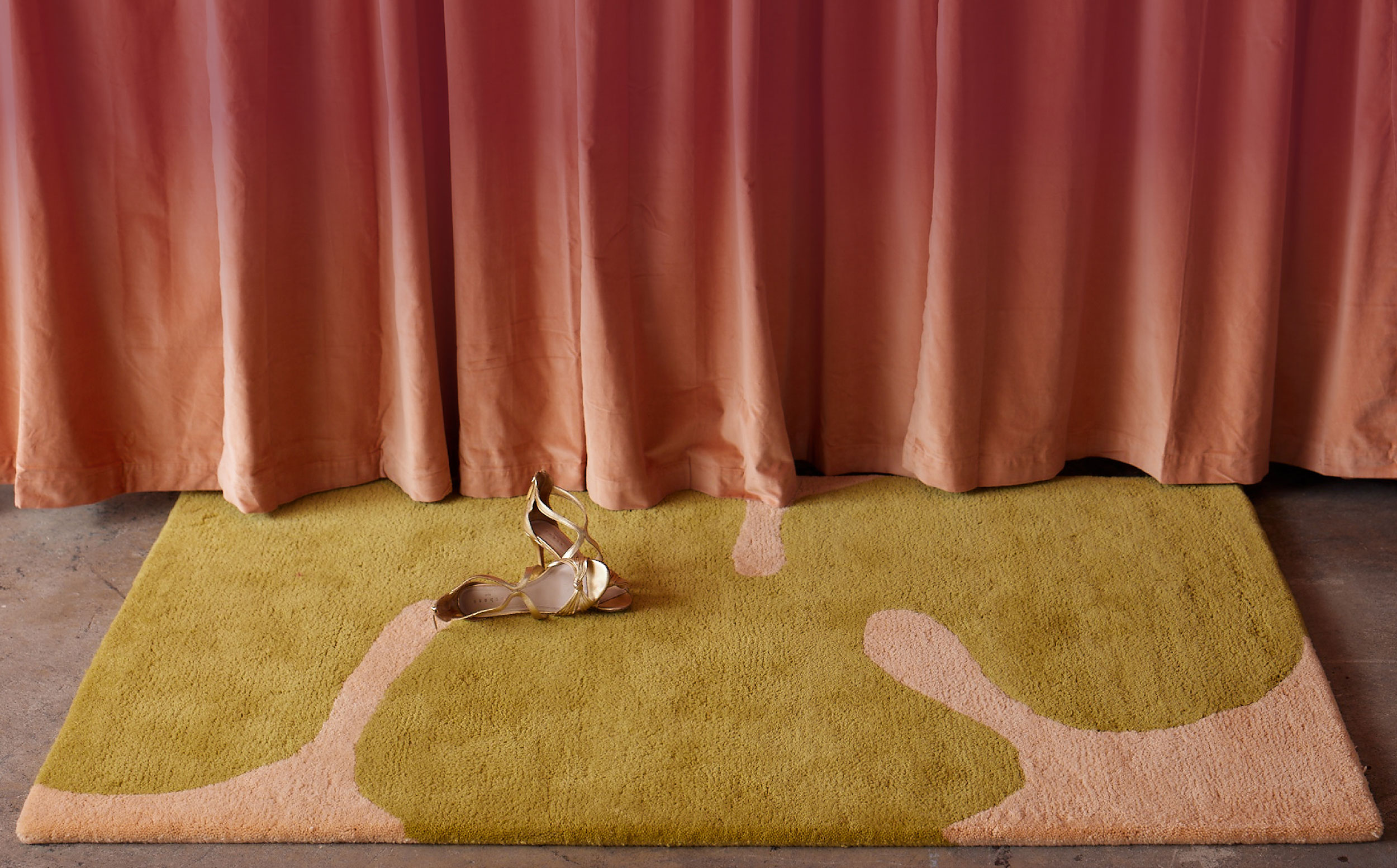 A plush area rug with modern shapes lays below a rose colored curtain
