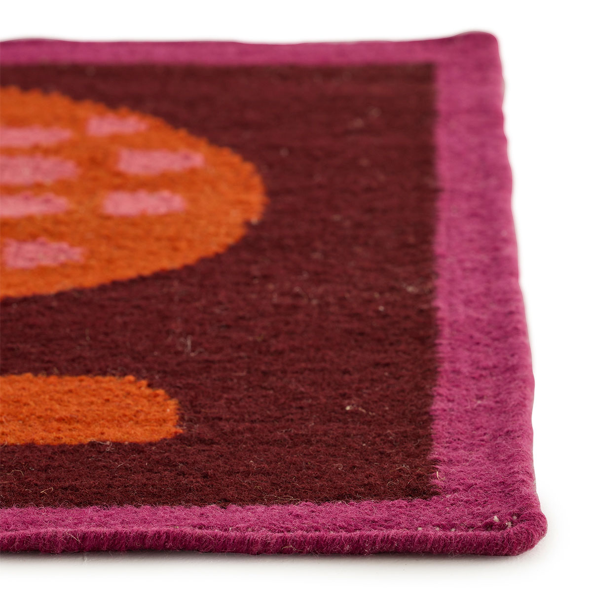 The corner of an abstract red and maroon rug called Happipod Berry.