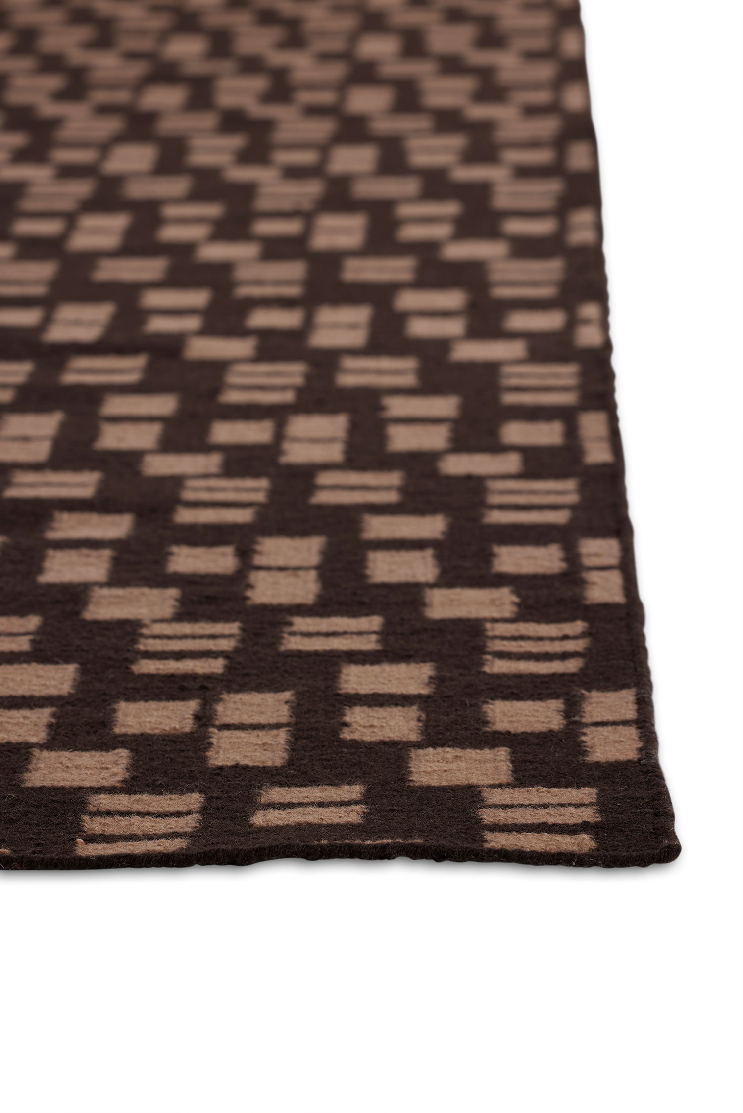 A close up of the corner of a jute area rug with tan rectangle patterns on a dark brown background.