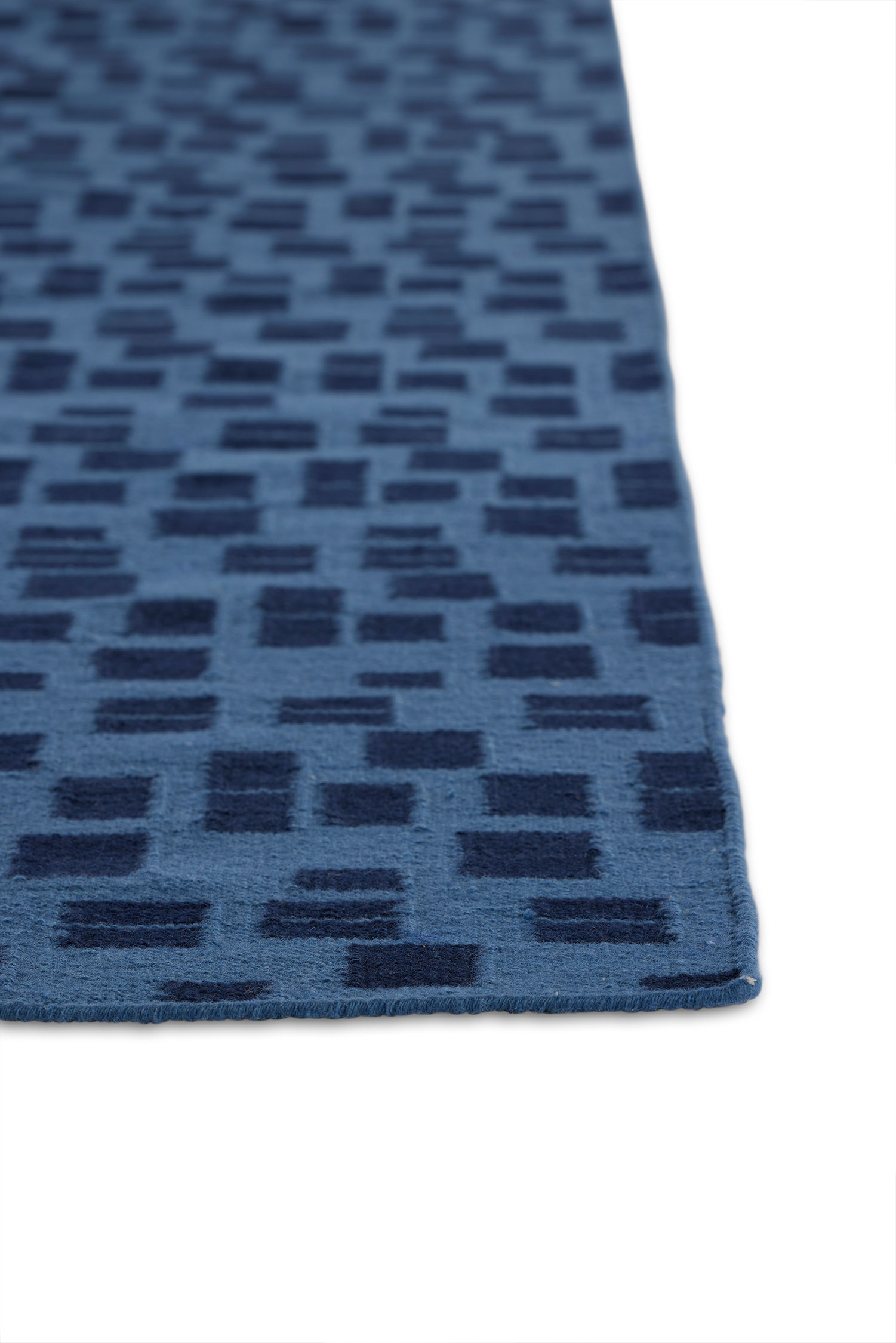 A close up of the corner of a jute area rug with blue rectangle patterns on a dark blue background.