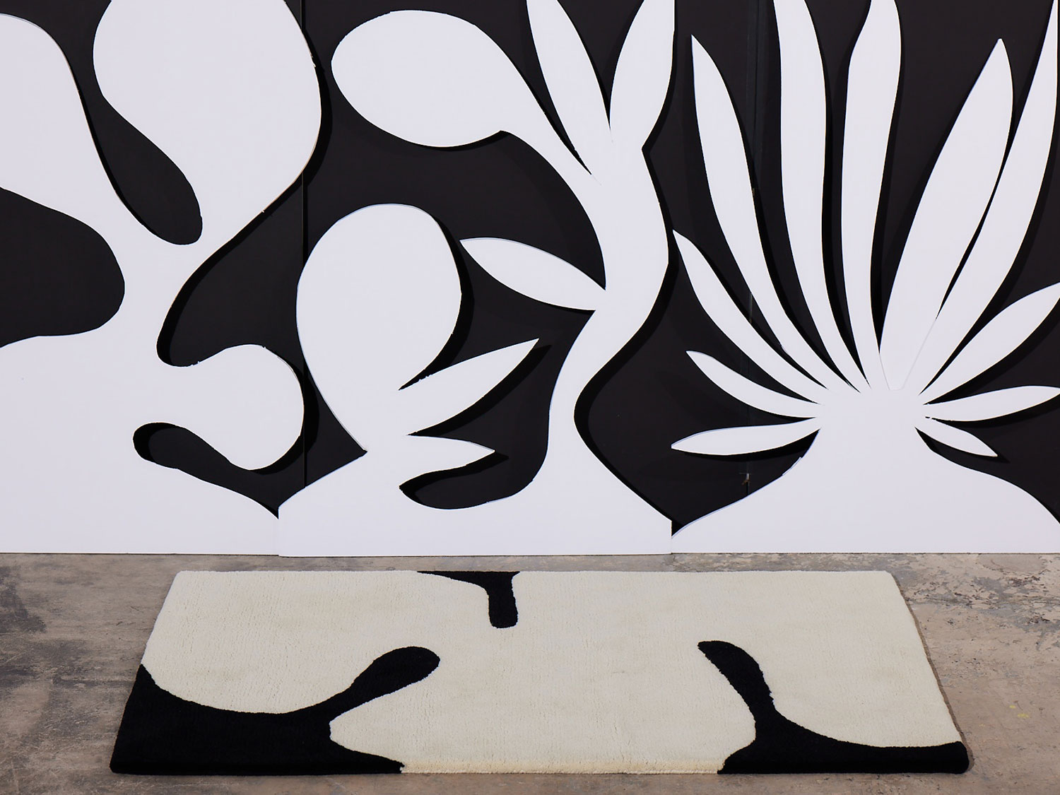 Astrud Coconut area rug by Angela Adams against a black and white patterned background