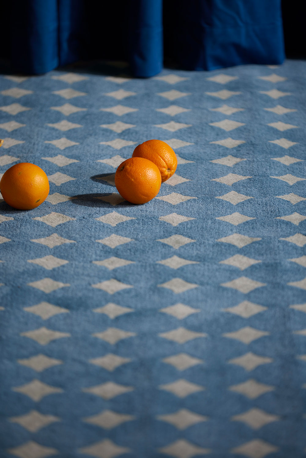 Another close up of oranges rolling on a blue area rug called Bongo Pool