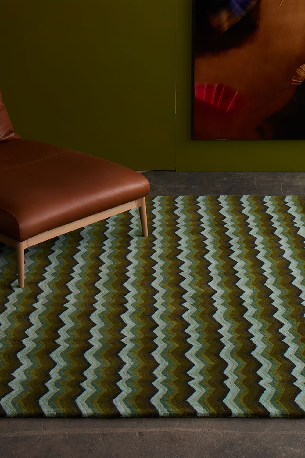 A modern area rug, with brown leather chair on it in green tones called Buzz Emerald