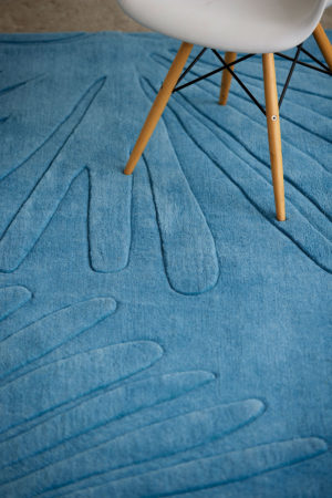A wooden chair sits on a modern area rug in blue called Daisies Sky