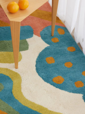 a wooden table on a multi-colored, modern area rug by Angela Adams called Daytrip Happy