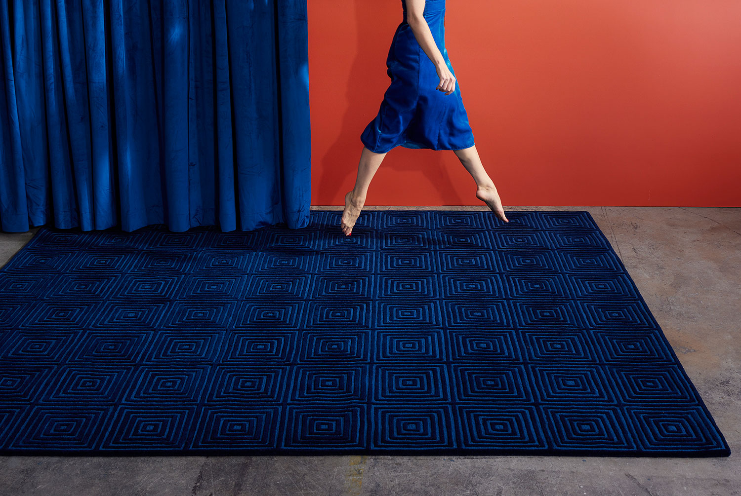 A woman skips across a deep blue, modern area rug called Duke Blue by Angela Adams
