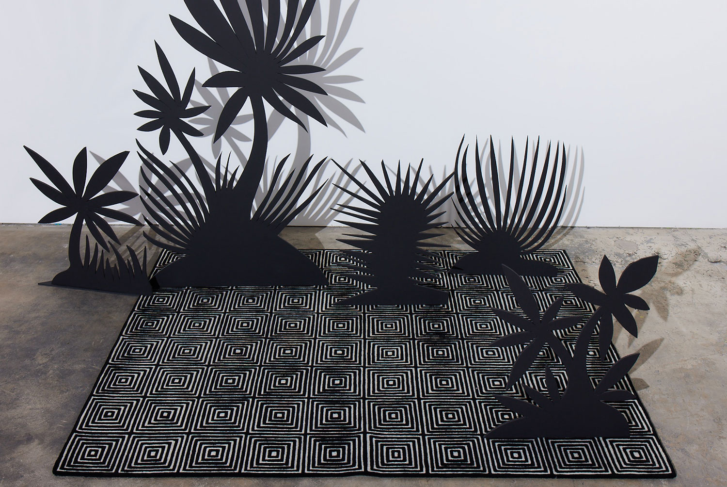 Black silhouettes of plants sit on a black and white, patterned, modern area rug called Duke Vivid by Angela Adams