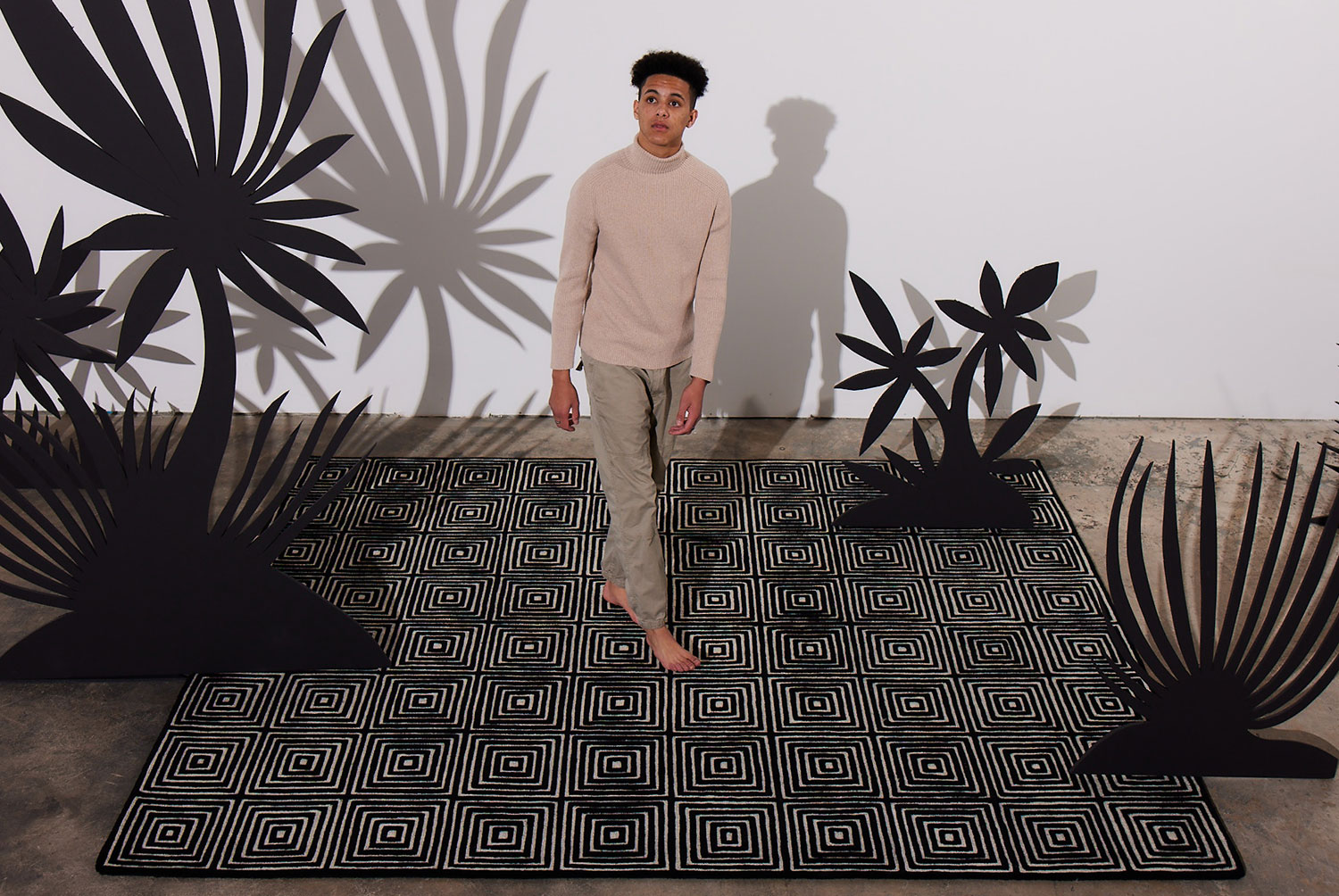 A man walks across a black and white, patterned, modern area rug called Duke Vivid by Angela Adams