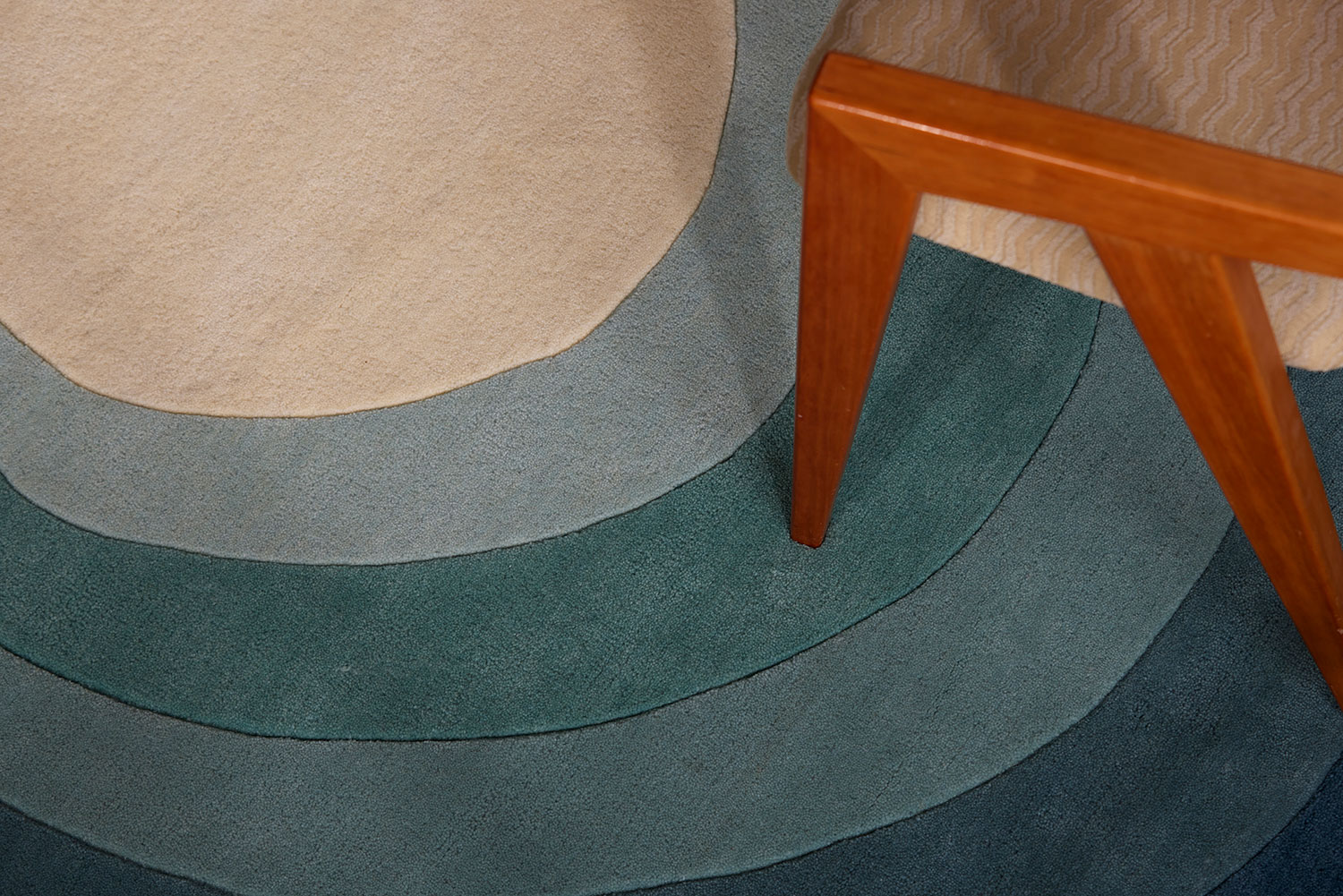A close up of a blue gradient area rug called Pool Dream in the shape of a pool with a wooden chair on it.