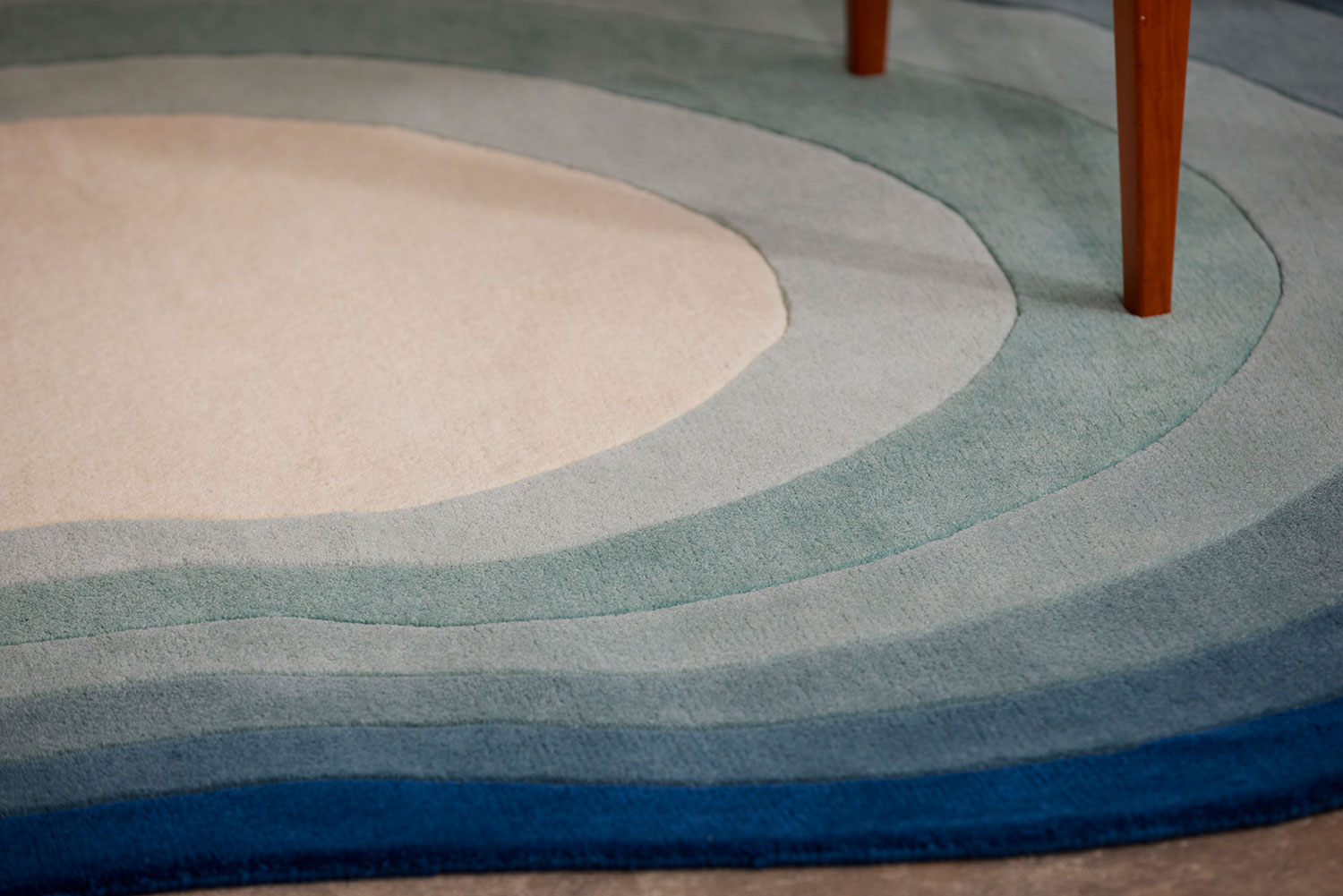 A close up of the edge of a blue gradient area rug called Pool Dream in the shape of a pool