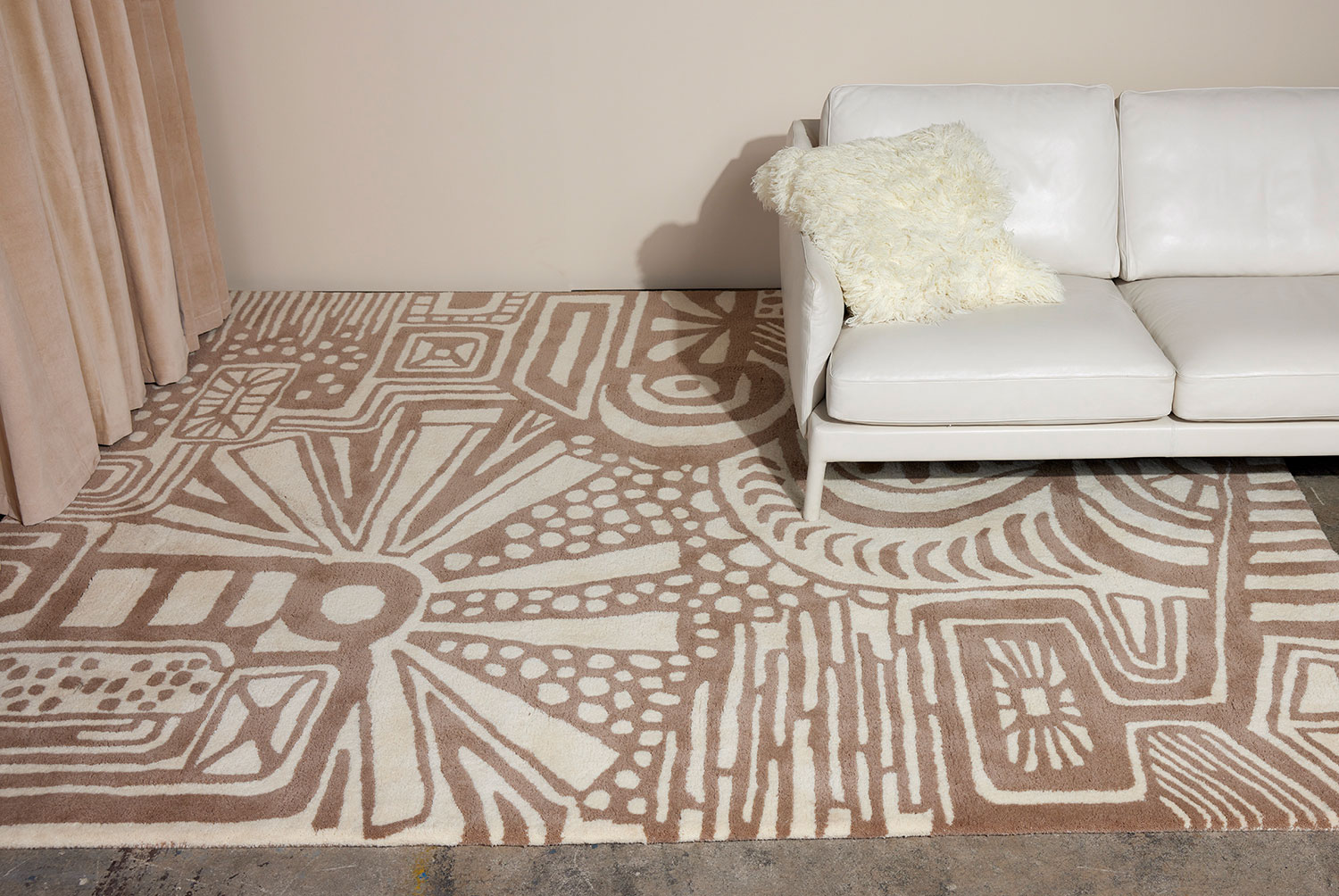 A white leather couch sits on a neutral colored, modern area rug called Storybook by Angela Adams