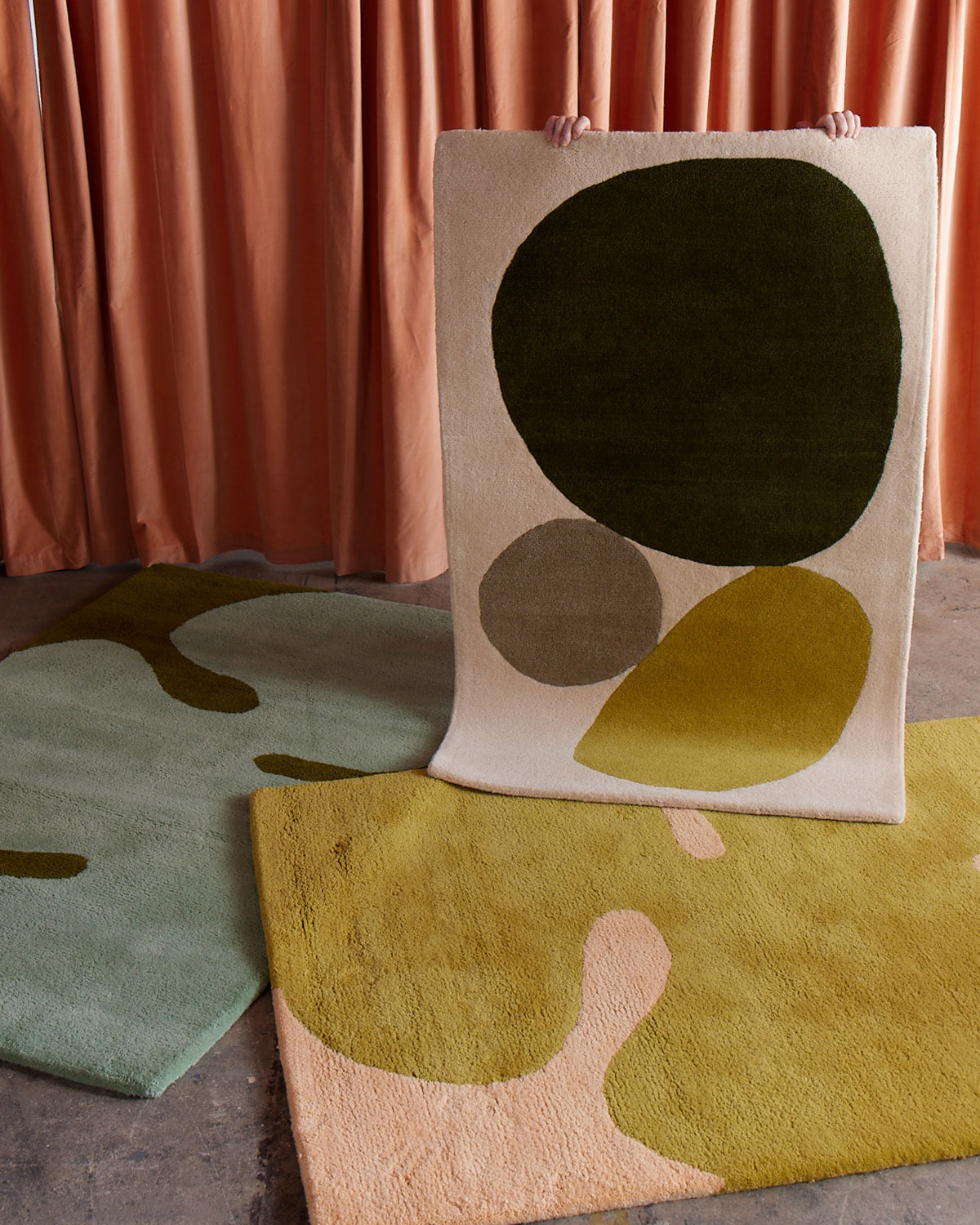 A 3 foot by 5 foot modern rug called Three Stones Moss is being held up by a person