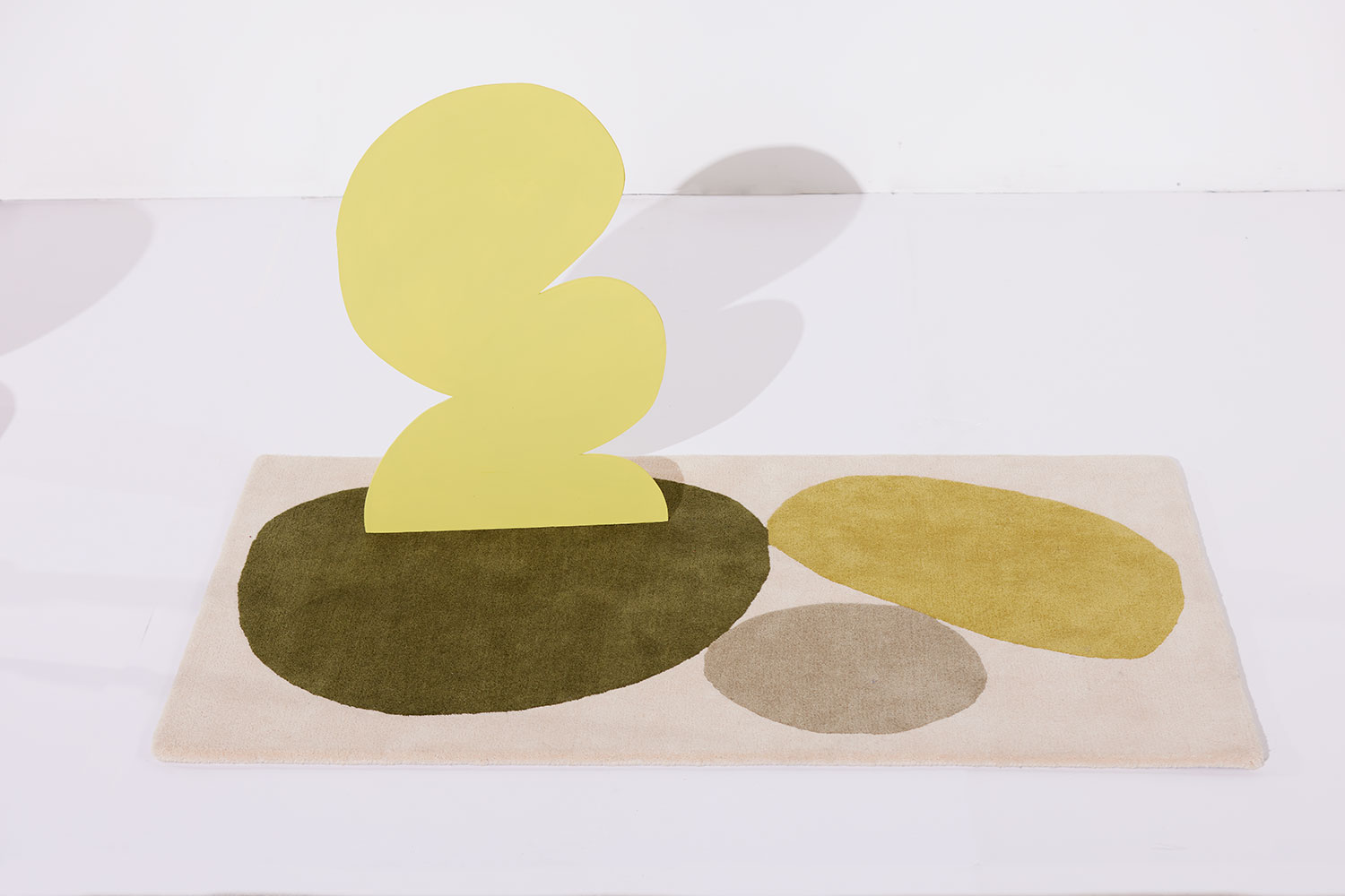 A yellow cardboard cutout sits on a 3 foot by 5 foot modern rug called Three Stones Moss