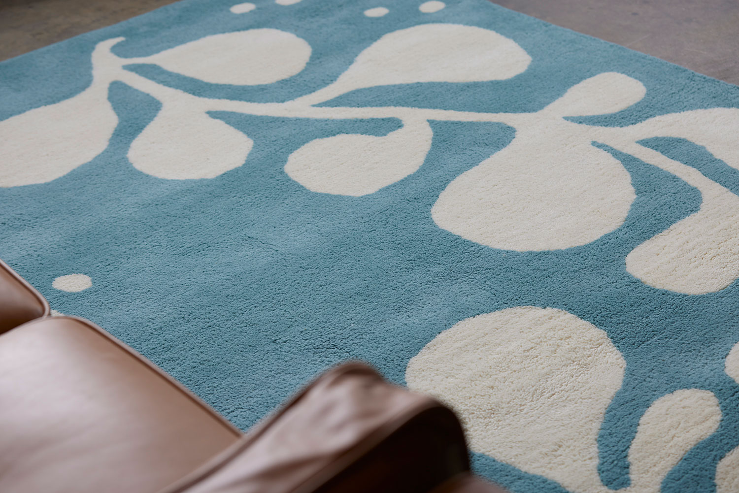 A brown leather chair sits on a neutral and blue area rug with abstract designs on it called Vine Hush