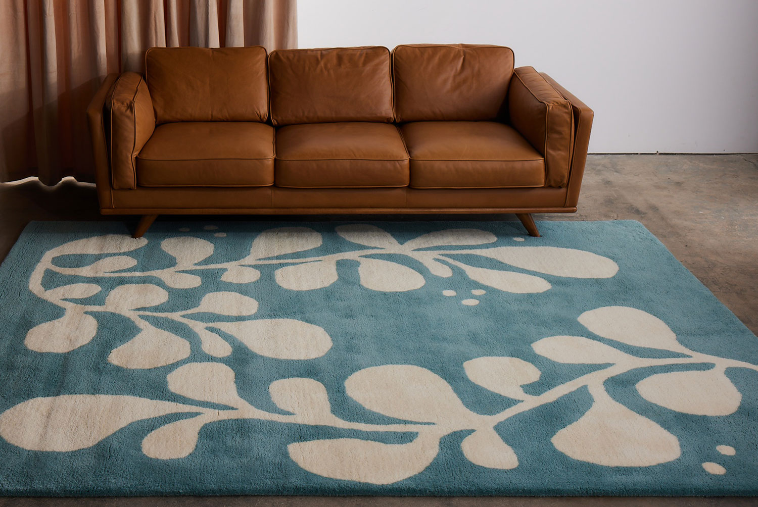 A brown leather chair sits on a neutral and blue area rug with abstract designs on it called Vine Hush