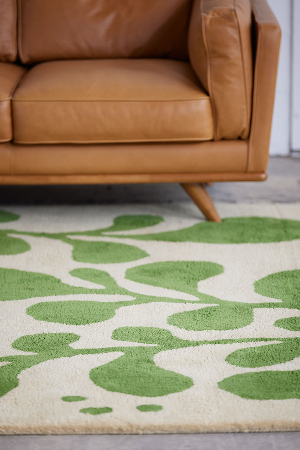 A brown leather chair sits on a neutral and green area rug with abstract designs on it called Vine Mambo
