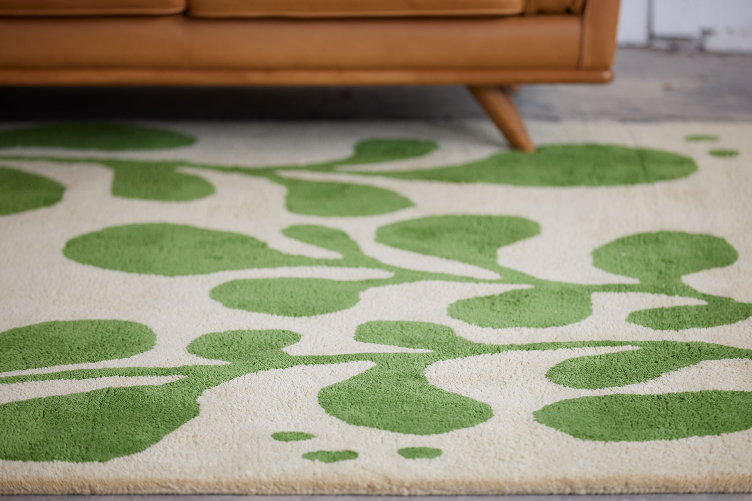 A brown leather chair sits on a neutral and green area rug with abstract designs on it called Vine Mambo