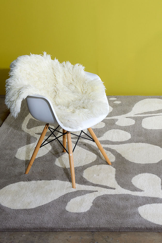 A white chair with a fuzzy bear blanket on it sits on a neutral and gray area rug with abstract designs on it called Vine Swoosh