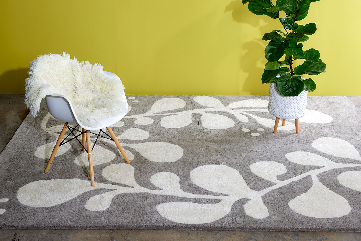A chair, and plant sit on a neutral and gray area rug with abstract designs on it called Vine Swoosh